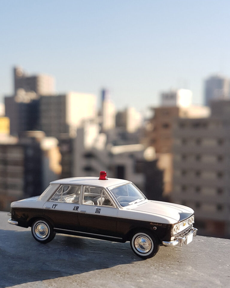 A classic die-cast sedan model with a city skyline behind it