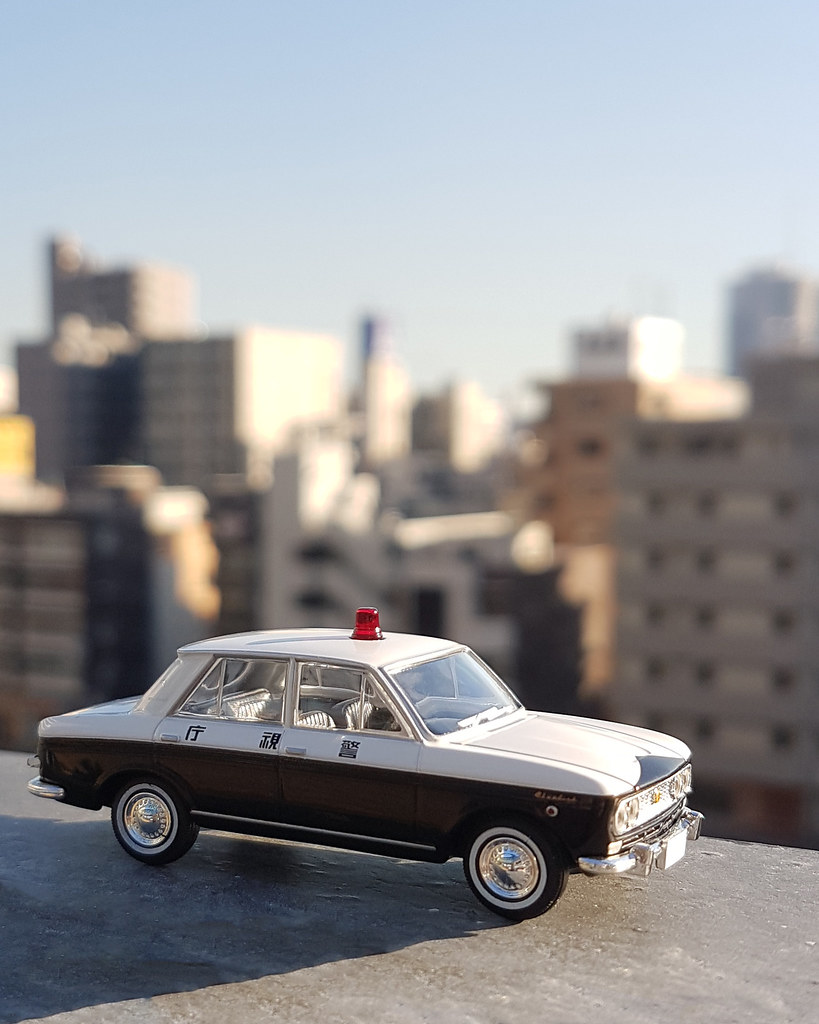 A classic die-cast sedan model with a city skyline behind it