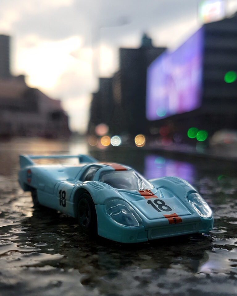 A die-cast race car model on a wet city street at dusk